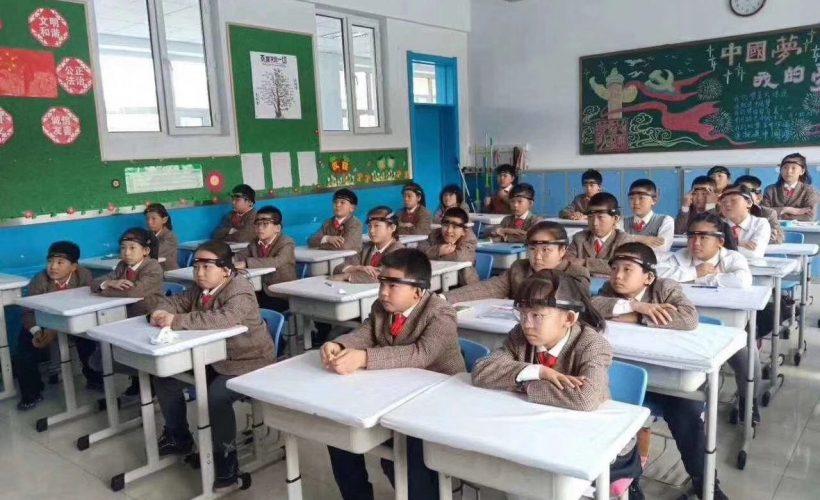 Chinese students wearing headbands sit at their desks in a classroom.