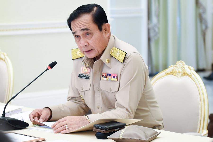 Thailand's Prime Minister Prayuth Chan-Ocha sits at a desk while speaking into a microphone.